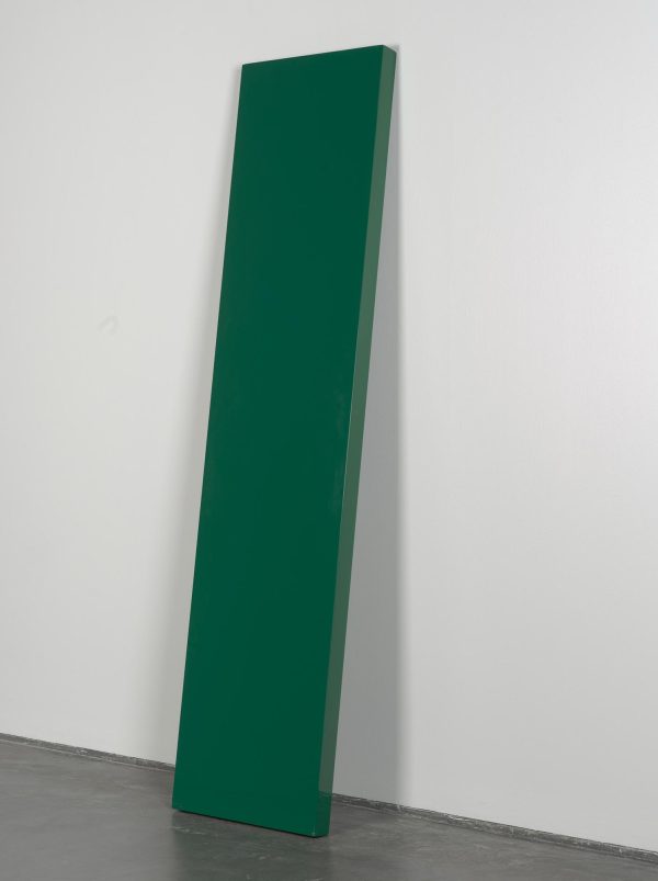 A forest green rectangular object leans against a white wall