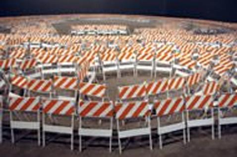 Blurry image of many orange and white striped construction barriers organized in several circular formations