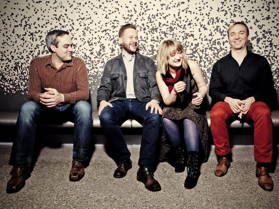 Four people sit on a bench, three of them looking towards the one furthest to the right