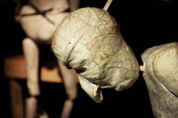 Close up of the head of a humanoid puppet made seemingly out of papier mache.