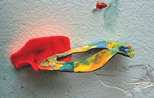 A pink form holds a ring of yellows, blues and oranges on a white drywall piece