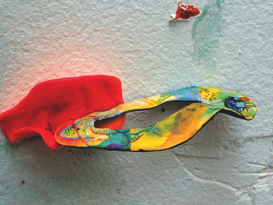 A pink form holds a ring of yellows, blues and oranges on a white drywall piece