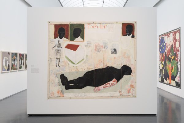 A large, unframed painting mounted to a free-standing wall depicts a horizontal nude figure with jet-black skin and one forearm exposed to reveal muscles and tendons. Other paintings are visible in the gallery behind the wall.