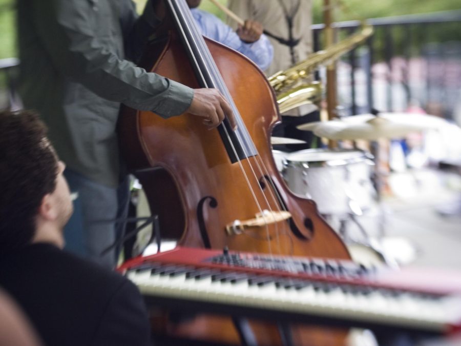 Closeup of a band playing in a row, the keyboardist in the foreground followed by the bassist and the drummer