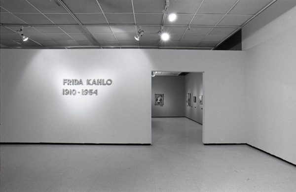 A false wall with a doorway to a room full of art on the walls displays the exhibition title: Friday Kahlo, 1910–1954