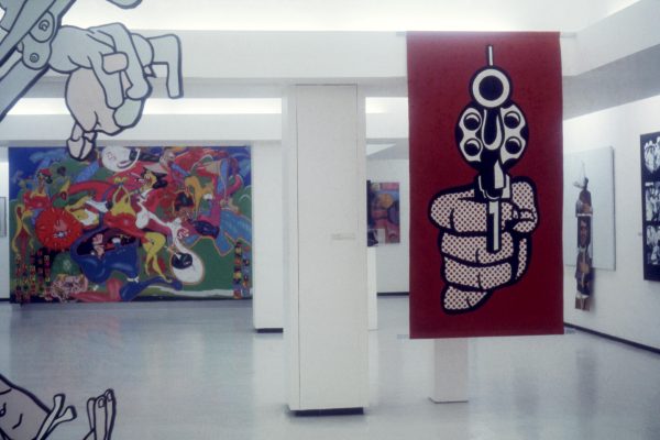 Artworks hang around a white gallery space. A pop art style image of a hand pointing a gun against a red background hangs from the ceiling.