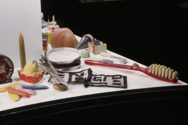 Several objects on the corner of a white surface, including a toothbrush, a scoop of ice cream, and a folded paper with the words 1st Ave, against a black backdrop