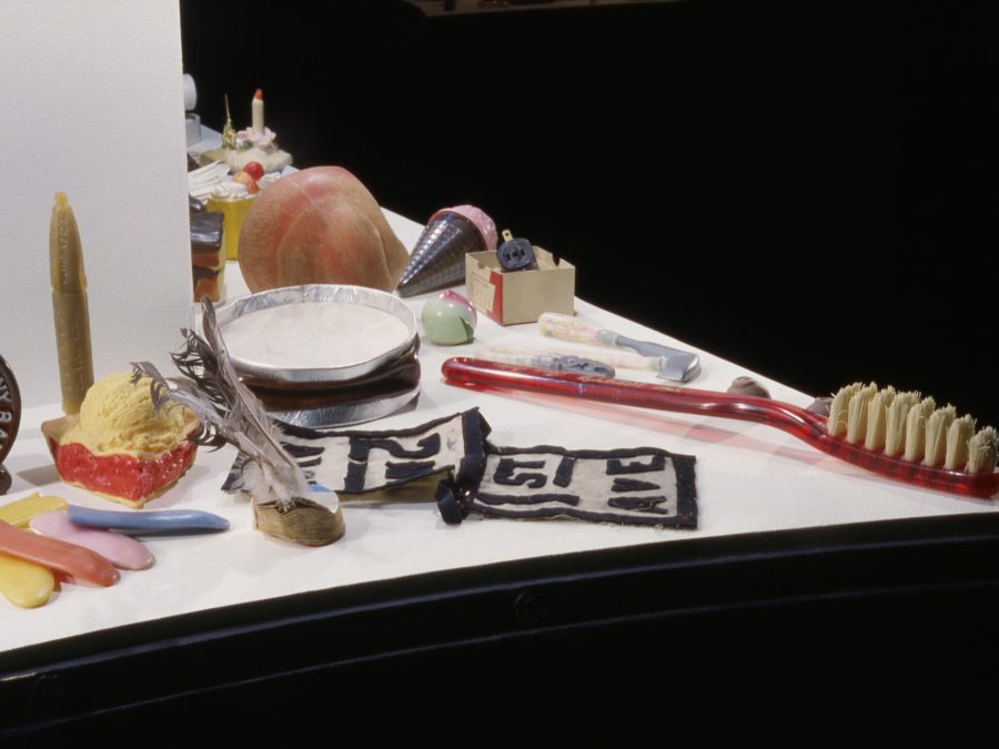 Several objects on the corner of a white surface, including a toothbrush, a scoop of ice cream, and a folded paper with the words 1st Ave, against a black backdrop