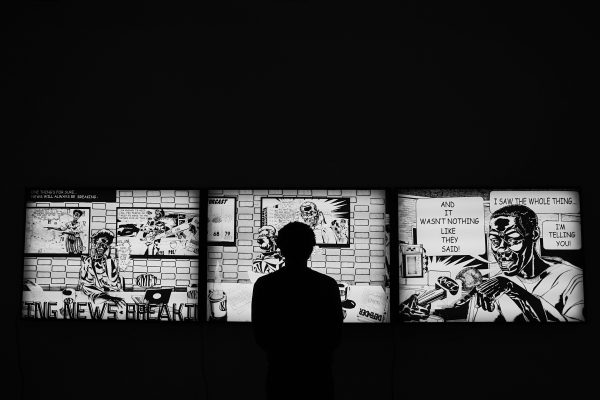 The silhouette of a person in front of a lighted three part comic strip in a dark room