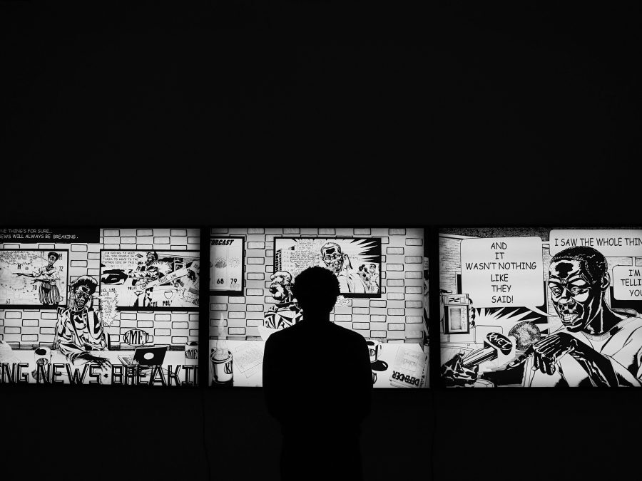 The silhouette of a person in front of a lighted three part comic strip in a dark room