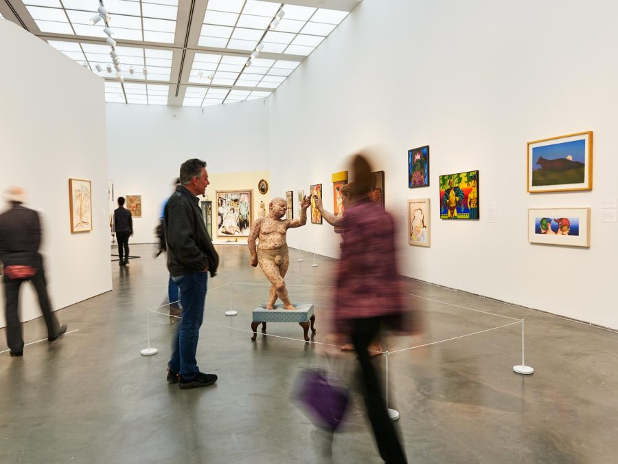 Several visitors look at paintings and sculpture in a gallery whose curvilinear walls draw viewers closer to its center.