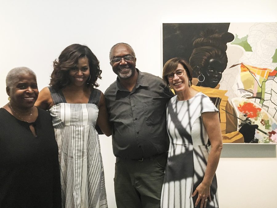 Four people pose next to a painting of a Black person painting a paint-by-number self-portrait
