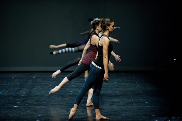 View down a row of dancers on a stage with their right legs extended backwards at varying heights.