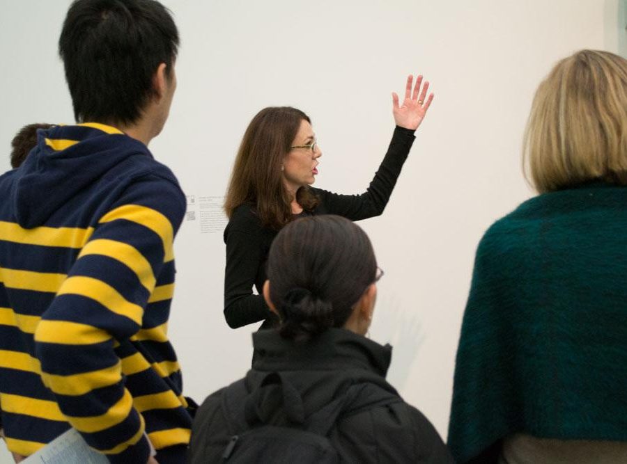 A female tour guide gestures to her left in front of several onlookers.
