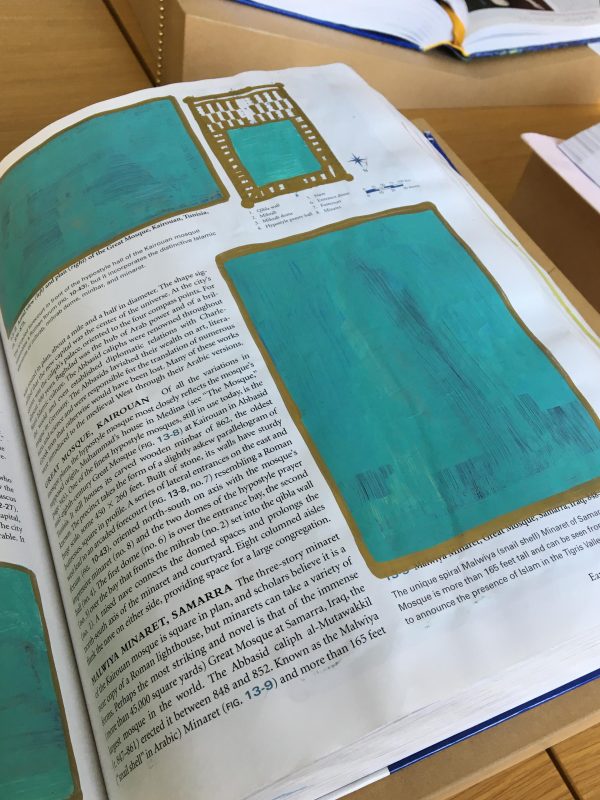 The right side of an opened book on a table with all images covered in teal paint with gold framing