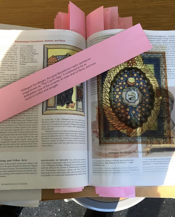 A pink slip of paper covers a portion of an open book featuring illustrations of art and a lot of text