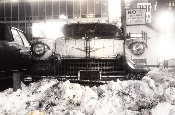 Archival photo of the front of an old Cadillac parked behind a dirty snow pile