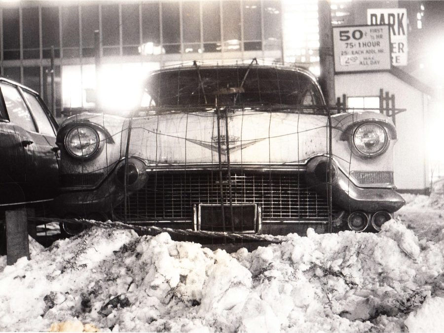 Archival photo of the front of an old Cadillac parked behind a dirty snow pile