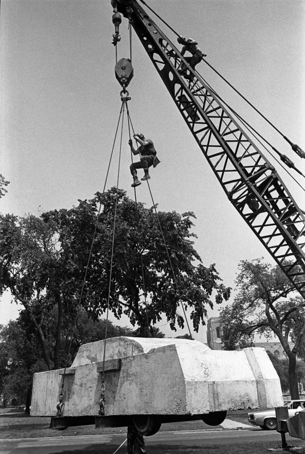 A black-and-white photo documenting a crane lifting a concrete car