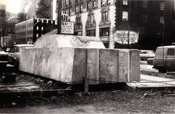 A large concrete block in the shape of a car with cars and buildings around it