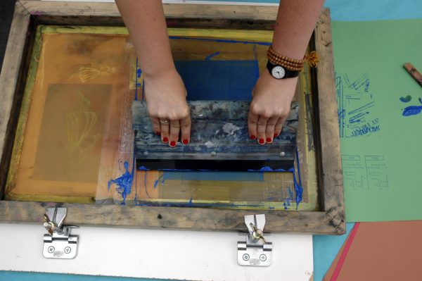 Two hands pull a squeegee across a screen printing frame