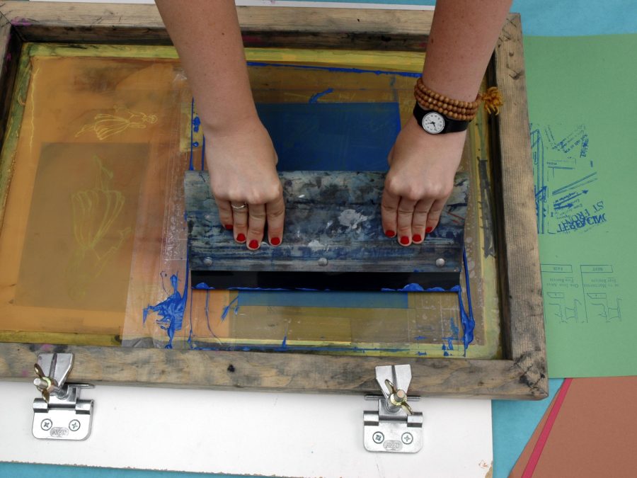 Two hands pull a squeegee across a screen printing frame