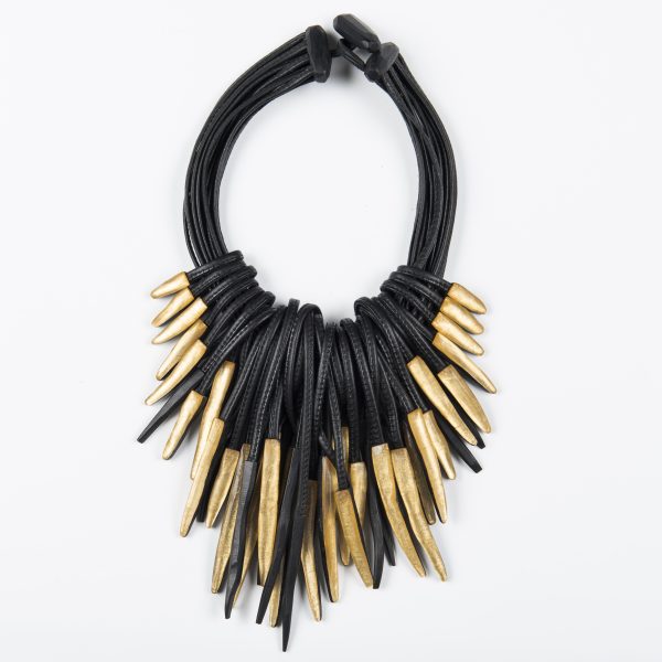 A necklace made from thick black leather cords features many gold dart-like pendants and fastens with a toggle at the top.