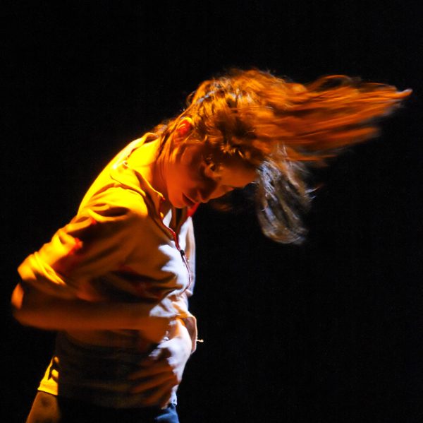An energetically dancing person flips their long hair.