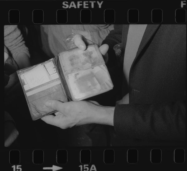 A black-and-white film frame shows hands holding an open wallet that contains faded photographs.