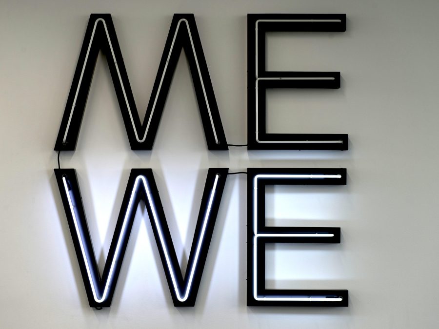 Neon light letters with black outlines that spell out Me on top and We on the bottom