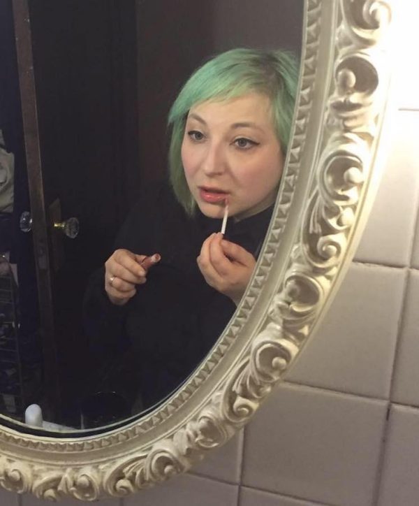 Photograph depicting the reflection of a young woman applying lip gloss in a decorative mirror.