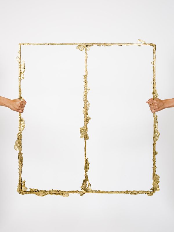 Two light-skinned hands seem to pull at opposite sides of a two paned gilded window frame