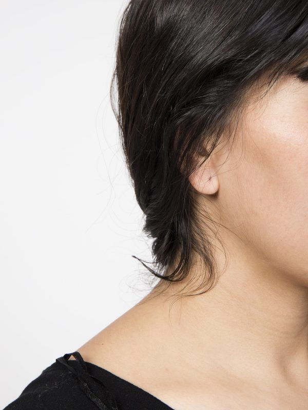 A photograph of part of a dark haired woman's head, revealing her neck, cheek, and jaw, with an obviously missing earring in her right ear.