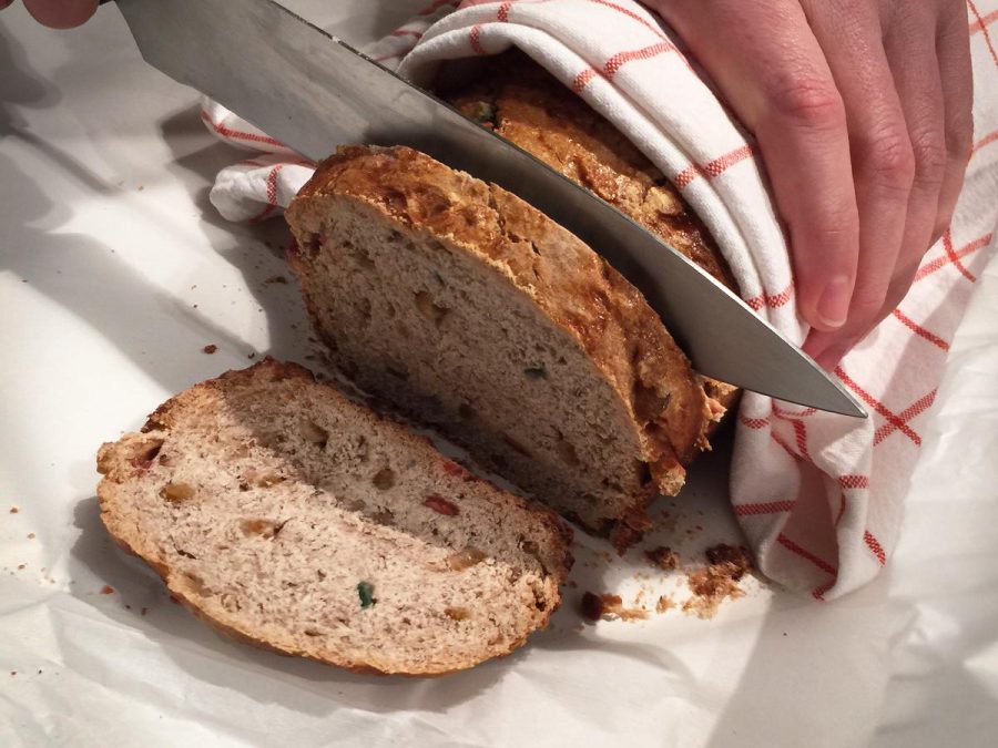 A person cuts a second slice of bread while holding the rest of the loaf with a towel