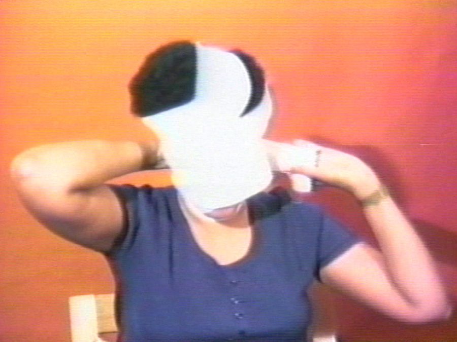 In this grainy image, a woman with a black afro is shown wrapping her face with a white bandage.