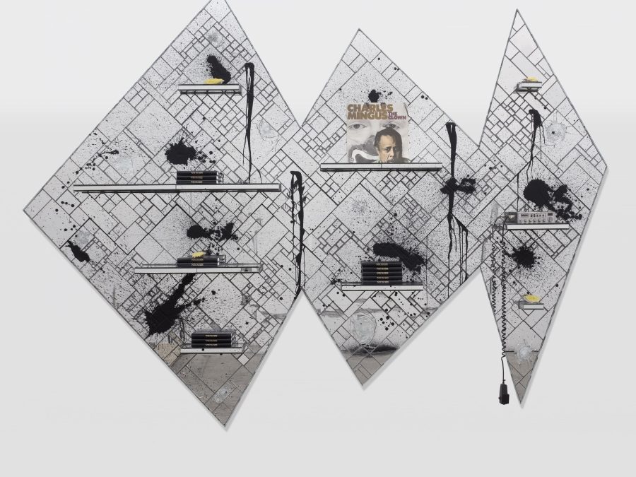 Three geometrically arranged diamond-shaped panels made up of tiled glass in various size rectangles and squares featuring shelves with piles of books on them, a Charles Mingus album, and an A-B radio. The whole thing is splattered with black.