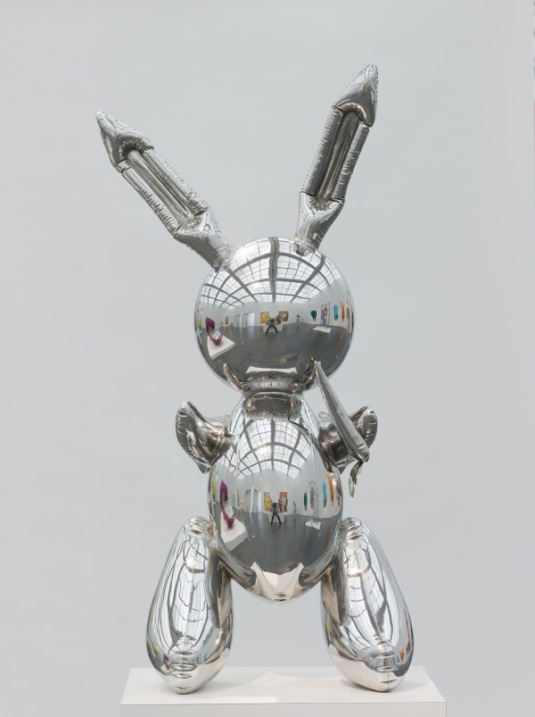 A sculpture that resembles a silver rabbit-shaped mylar balloon stands on a pedestal. A museum gallery is visible in the sculpture's reflective surface.