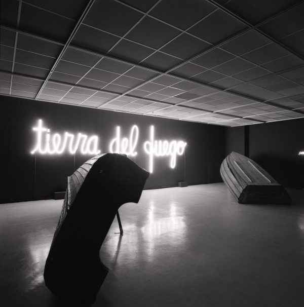 Neon lights spelling out tierra del fuego illuminate an otherwise dark room containing an overturned boat and another large object