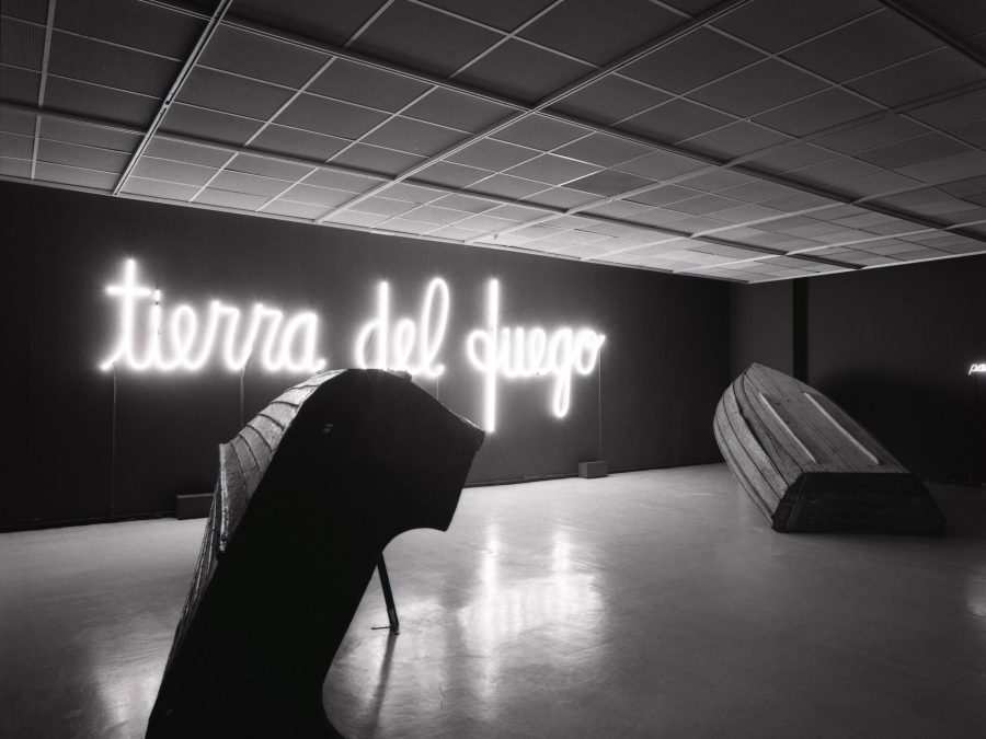 Neon lights spelling out tierra del fuego illuminate an otherwise dark room containing an overturned boat and another large object
