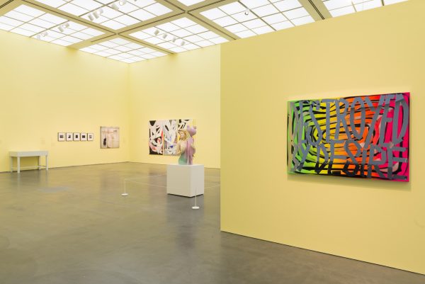 A gallery space painted sherbet yellow with artworks hanging on the walls and sitting on podiums