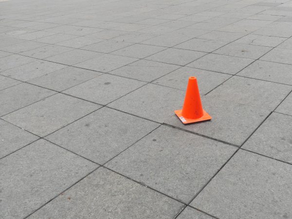 A lonely orange hazard cone sits on a grid of gray tiles.