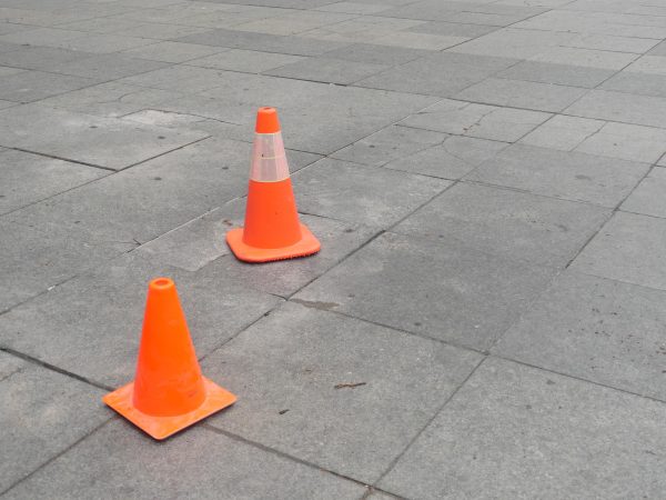 Two orange hazard cones appear on a gray, tiled surface. One is bigger than the other and has a reflective stripe.