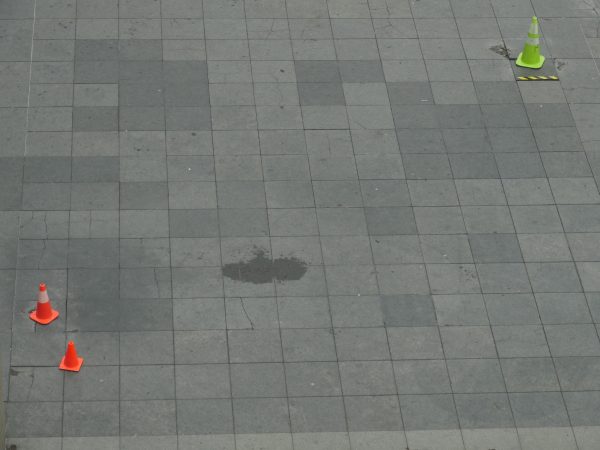 Three traffic cones, two orange, one green, on a stone plaza