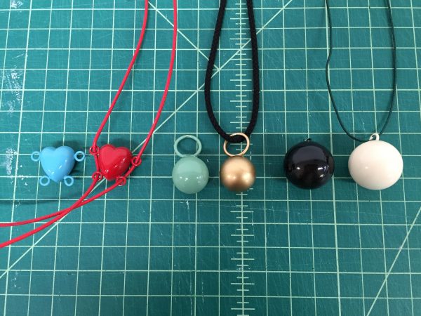 Pendant necklaces in blue and red hearts, and seafoam green, gold, black, and white balls against a green grid cutting mat