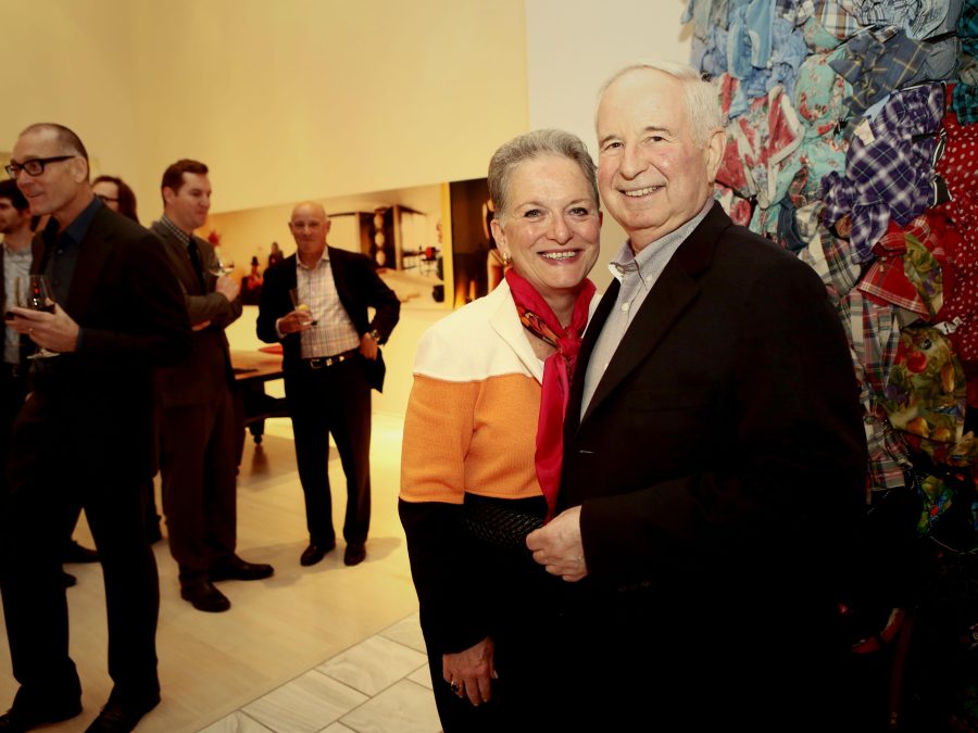 Two people with pale pink skin pose in a gallery among art and other people