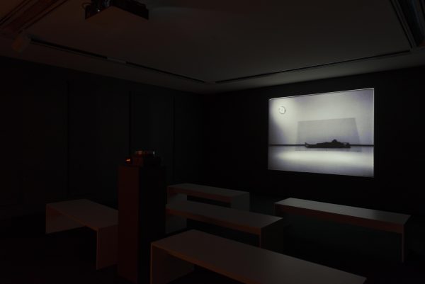 A dark room with a projection of Chris Burden's performance art piece 'Doomed'