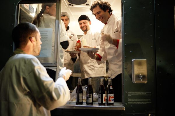 A person stands outside a food truck filled with a four-person crew