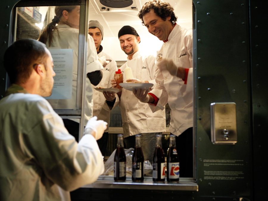 A person stands outside a food truck filled with a four-person crew