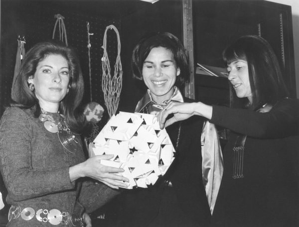 Vintage black and white image of three women holding a geometric sculpture in front of a display of jewelry