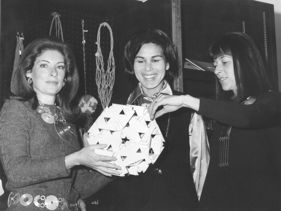 Vintage black and white image of three women holding a geometric sculpture in front of a display of jewelry